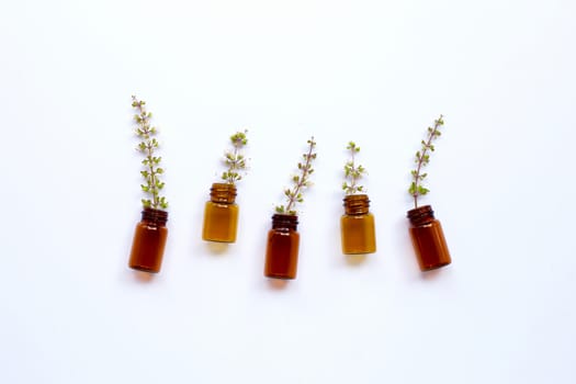 Empty essential oil bottles with holy basil flower on white background.