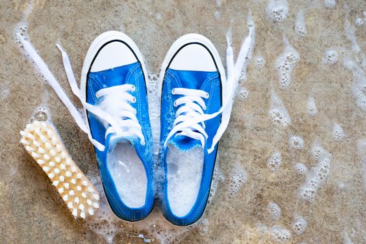 Sneakers with foam of powder detergent water dissolution and wooden brush on cement floor. Washing dirty shoes. Top view