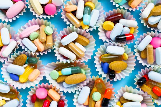 Colorful tablets with capsules and pills in cupcake wrappers on blue background.