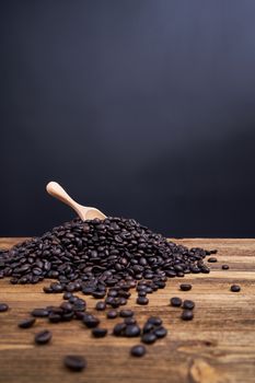 Wood spoon put on pile of coffee bean overflow on old wooden table with black background and copy space.