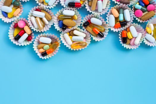 Colorful tablets with capsules and pills in cupcake wrappers on blue background.