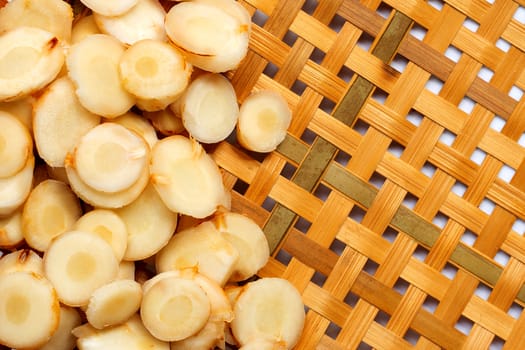 Fresh galangal slices on wooden bamboo threshing basket background. Top view