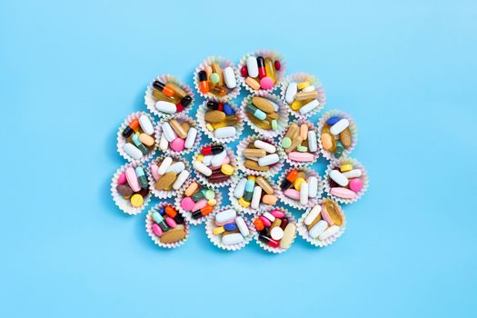 Colorful tablets with capsules and pills in cupcake wrappers on blue background.