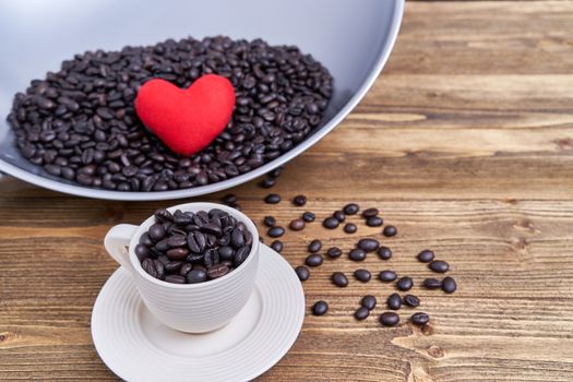 Close up coffee bean in white cup with saucer on old wooden table have blur heart on pile of coffee bean in pan and copy space.