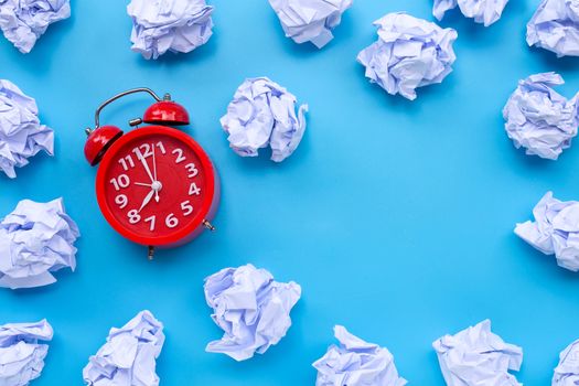 Red alarm clock with white crumpled paper balls on a blue background. Top view