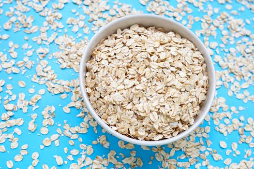 Oat flakes in bowl on blue background. Healthy food concept