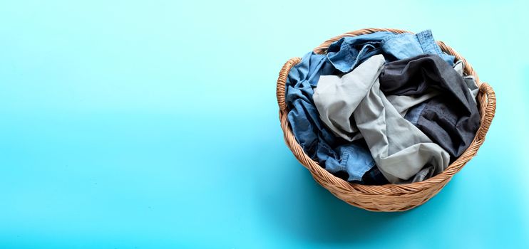 Clothes in laundry basket on blue background. Copy space