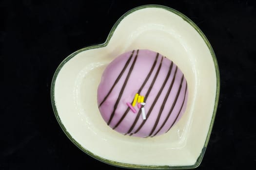 a pink donut on a heart-shaped ceramic plate, dark background