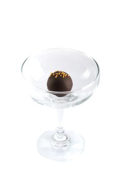 a small chocolate ball with dark swiss chocolate filling and small gold sugar drops, in a clear glass, isolated on white background, top view, minimal design