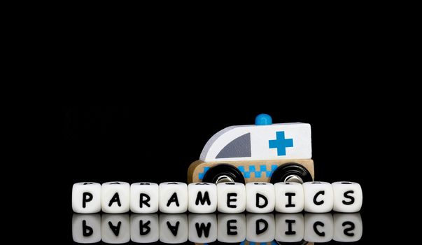 Alphabet letters spelling a word paramedics with a model ambulance in the background. Medical emergency concept