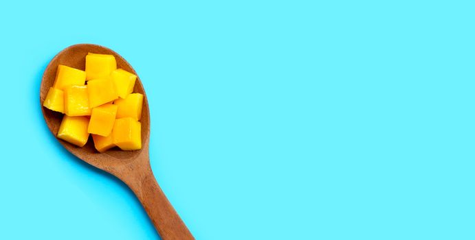 Sliced ripe mango cubes on wooden spoon on blue background. Copy space