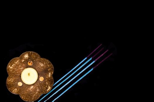 a scented candle on a coconut shell and some blue incense sticks on dark background, oriental simplicity concept