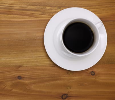 a white porcelain coffee cup and a saucer with black coffee on wooden background