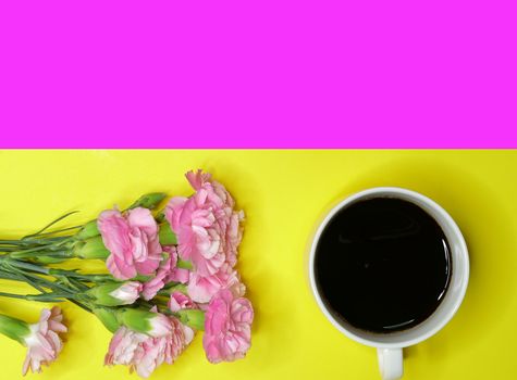 A cup of black coffee and a branch of beautiful pink carnations on a yellow and magenta background. Directly above, flatlay with empty space.