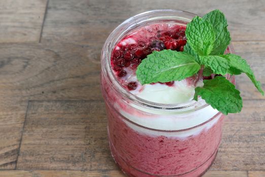 Chilled mixed berry smoothie in a large glass jar with mint sprig. Closeup, wooden background.