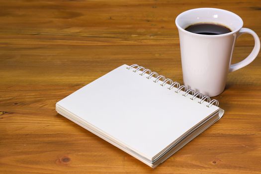 a white spiral notebook and a white coffee mug on a brown wooden table
