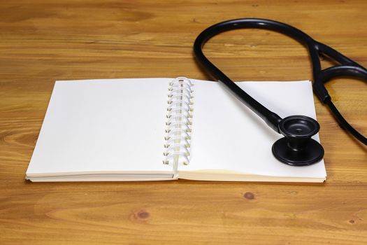 a black stethoscope and a white spiral notebook, on a brown table, top view