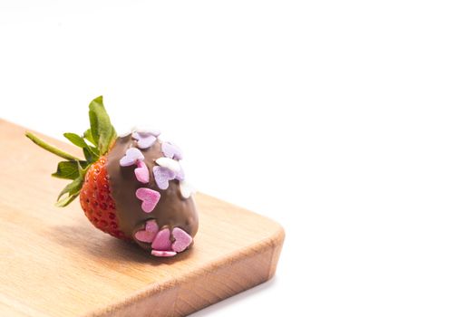 a chocolate coated strawberry with small heart-shape sugar confetti, on a brown wooden cutting board isolated on white background, Valentine