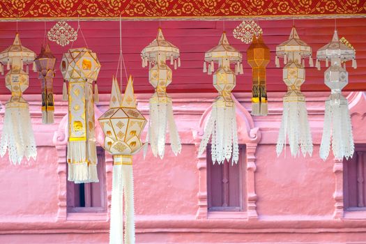 Traditional perforated design northern Thai style paper lanterns hanging from the temple ceiling as relgious offerings, typically decorated with elaborate golden elephant or other zodiac animal signs and patterns