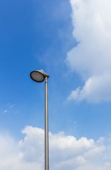 Modern streetlamp of round shape on a blue sky with some clouds.
