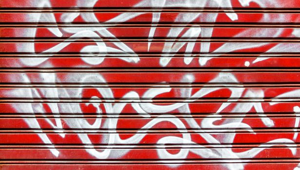 Red garage gate with vandalism sign of graffiti white spray paint. Ideal for concepts and backgrounds.