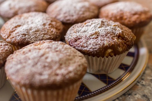 Batch of homemade freshly baked cupcakes or muffins cooling on a decorated plate, in the kitchen in a close up view with selective focus.