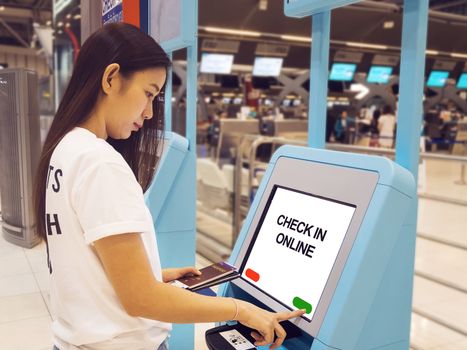 young Asian woman with passport using self check-in kiosk touch screen interactive display in airport, doing self check-in for flight or buying airplane tickets at automatic device in airport terminal
