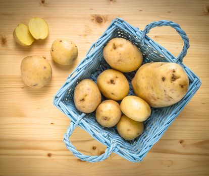 Fresh potatoes in wooden vintage basket on old table as background. Top view