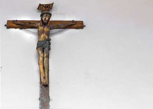 Small old wooden crucifix on a wall white as a background, with free space for text.