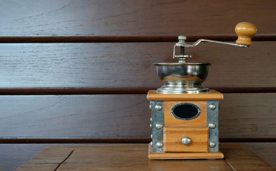 vintage coffee grinder with a metal bow on a wooden table and wall background