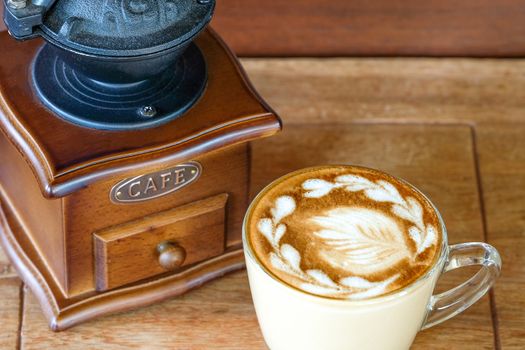 a cup of warm latte on a small wooden table with a vintage coffee grinder