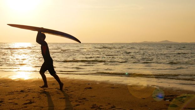 silhouette of happy surf man running with long surf boards at sunset on tropical beach. surfer on the beach in sea shore at sunset time with beautiful light. surfing for water sport outdoor activity