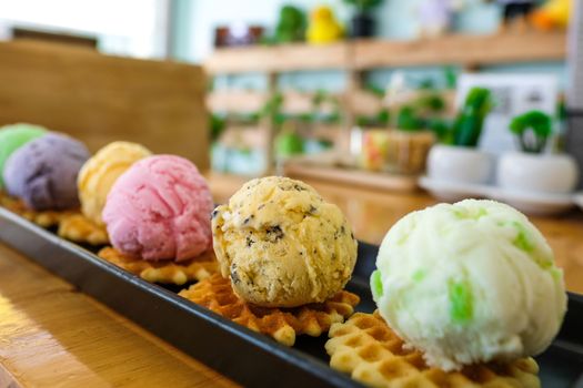 Multi colored and multi flavored ice cream on peices of waffle. Top view shot. Wood table background.