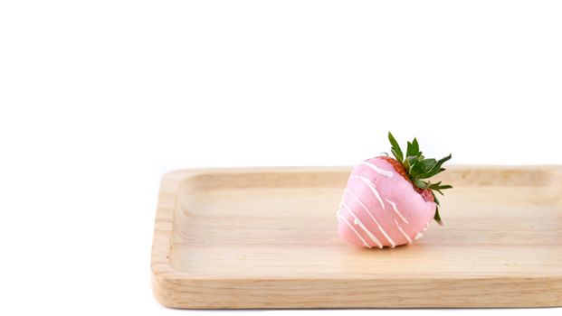 A pink chocolate coated strawberry on a wooden tray, isolated on white background