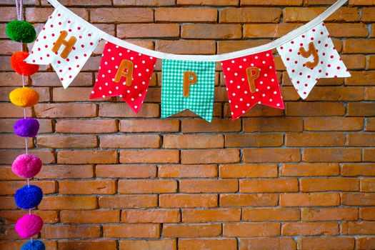 a beautiful and colorful cloth banner showing a word happy on a brown brick wall