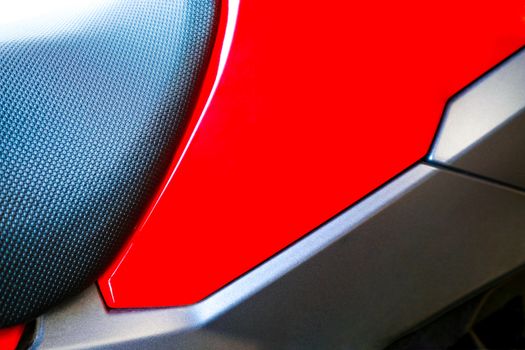 close up image of a motercycle seat showing contrasting colors and textures of its red and black components, the vehicle is generic looking and its model cannot be identified