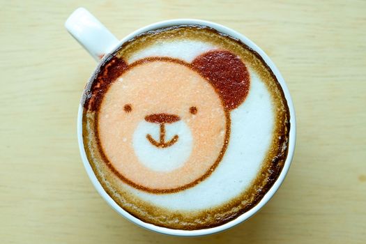 hot coffee in a white ceramic cup with cute bear face latte art, wooden background
