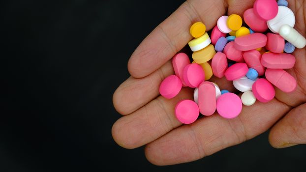 a person holding out a handful of pills. closeup, dark background