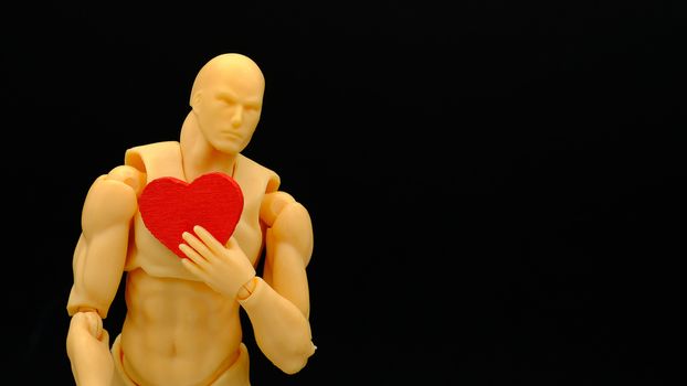 a human model holding a piece of wooden red heart , isolated on black background