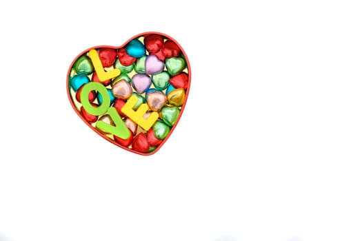 heart-shaped chocolate candies in various colors in a heart-shape tin box together with letters spelling LOVE, Valentines' Day, romantic concept, top view, isolated on white, with copy space