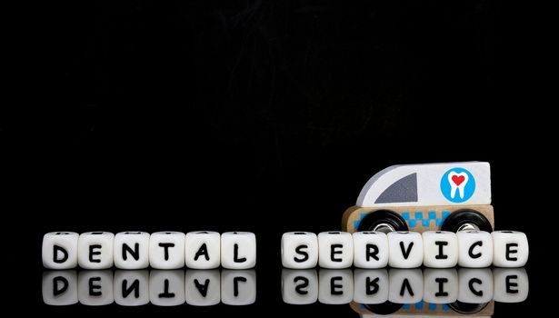 Alphabet letters spelling a word dental service with a model ambulance in the background. Ambulatory dental service concept.