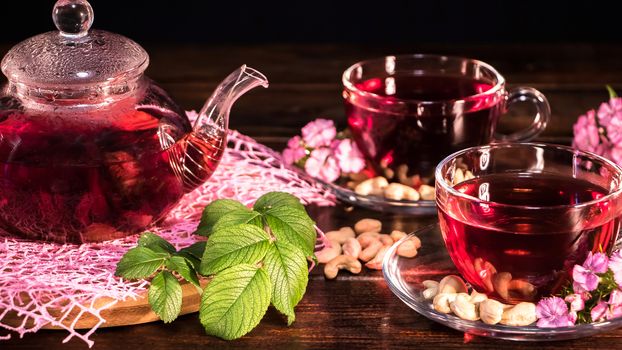 Hot luxury tea with a pleasant smell in a cozy home.Relaxing drink.Teapot, mugs of tea, cashew nuts, clove flowers and green medicinal leaves. Tea ceremonies and traditions in Japanese and Zen style