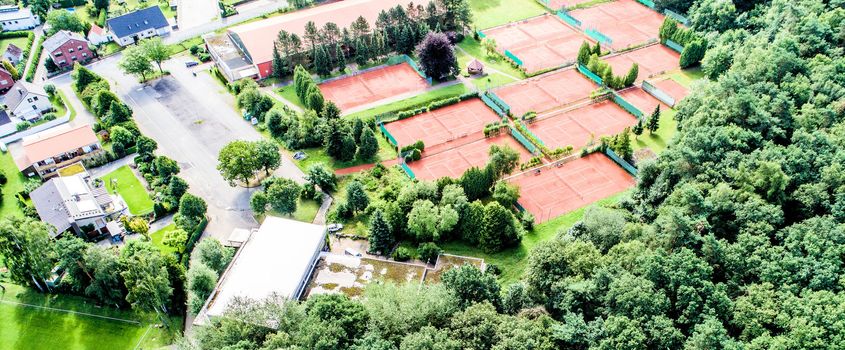 Aerial view of ten tennis courts in a forest