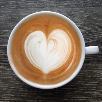 Top view of a mug of latte art coffee on timber background.