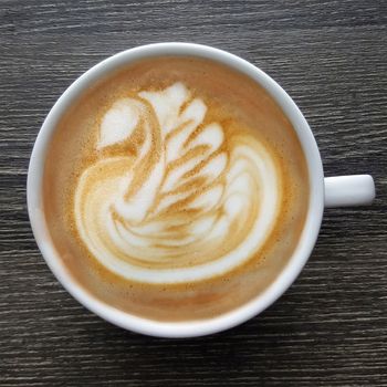 Top view of a mug of latte art coffee on timber background.