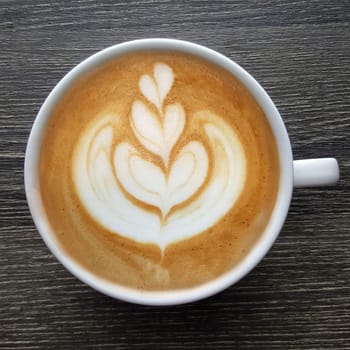 Top view of a mug of latte art coffee on timber background.