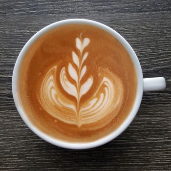 Top view of a mug of latte art coffee on timber background.