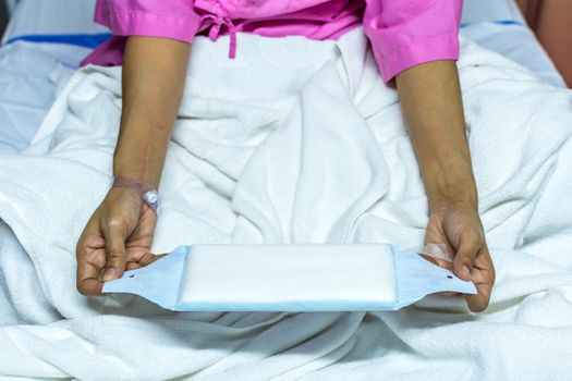 Patient asian woman with adhesive plaster on hand using sanitary napkin for menstruation on patient bed in the hospital