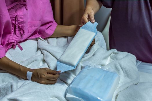 Patient asian woman with adhesive plaster on hand using sanitary napkin for menstruation on patient bed in the hospital