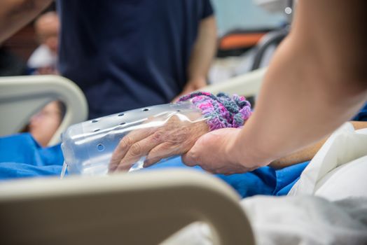 Patient in the hospital with saline intravenous and relatives patient hand holding a elderly patient hand with DIY restraint gloves